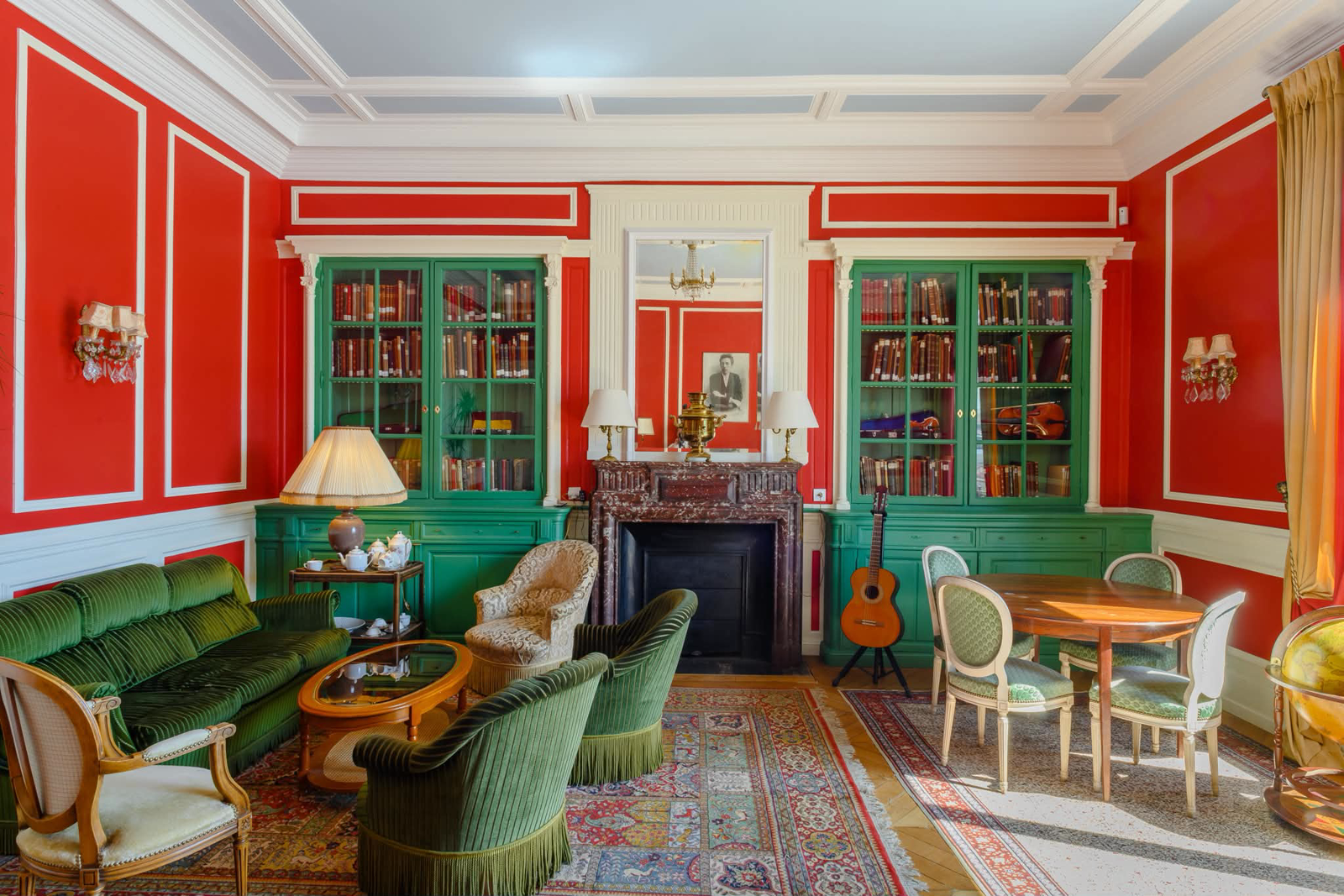 Salon de bibliothèque aux boiseries vertes et murs vermillon, mobilier d'époque